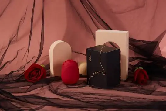 A red rose-shaped device and a dark gift box arranged with roses and draped fabric
